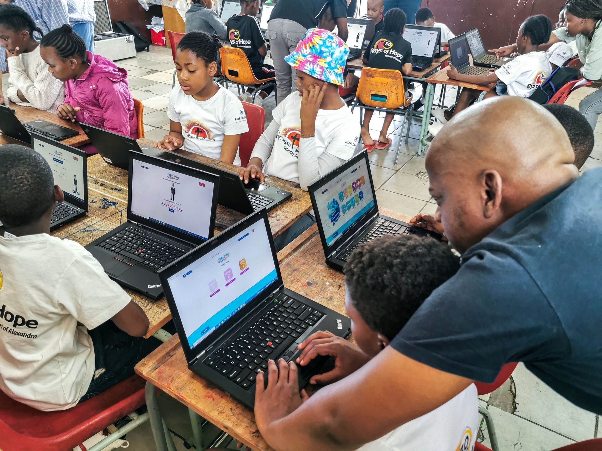 Children using laptops in a classroom setting, guided by an adult instructor.